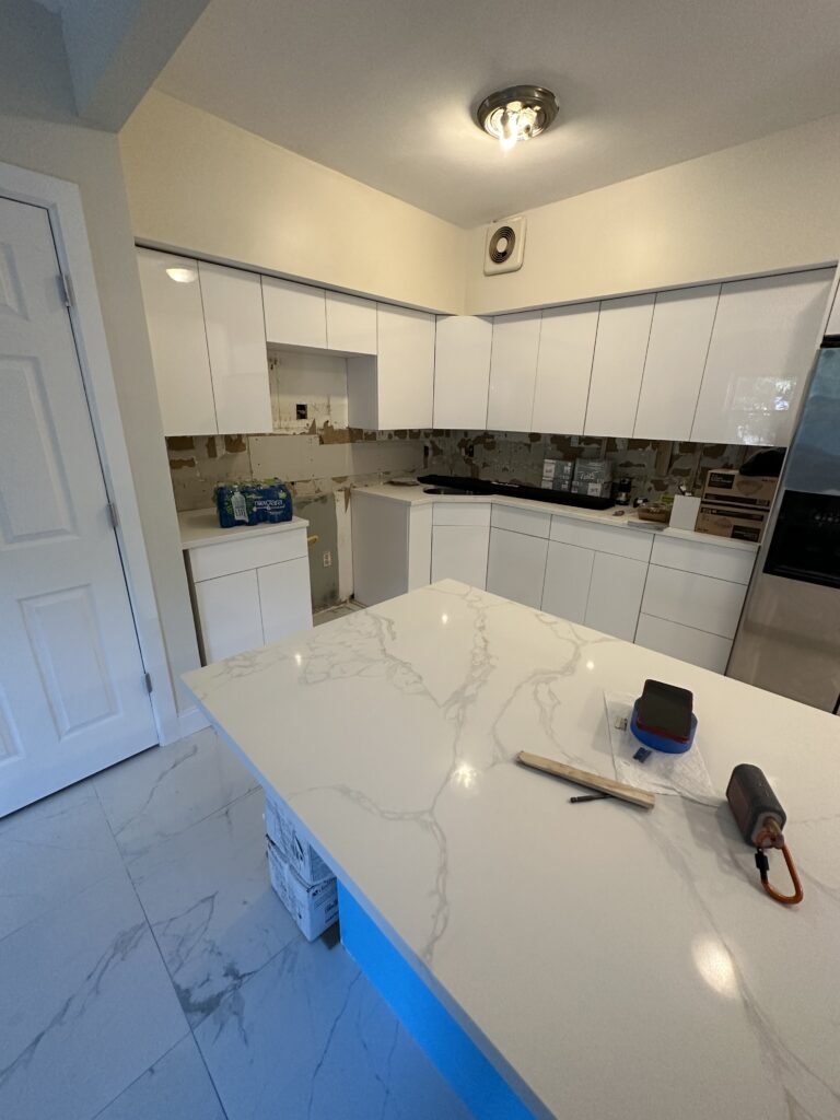 Before Image:
Old kitchen with wood cabinets, dark countertops, and outdated layout before renovation
After Image:
Modern kitchen with white custom cabinets, island, tile flooring, and updated lighting