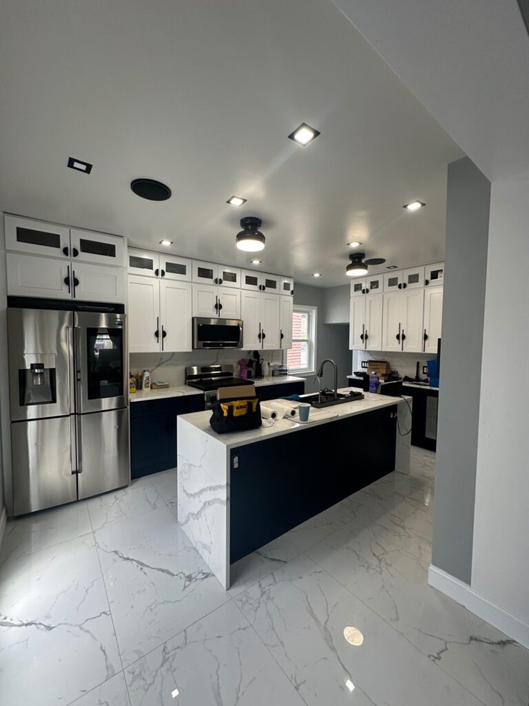 Modern kitchen remodel featuring white shaker cabinets, quartz waterfall island, stainless steel appliances, and marble tile flooring installed by DLS Construction LLC.